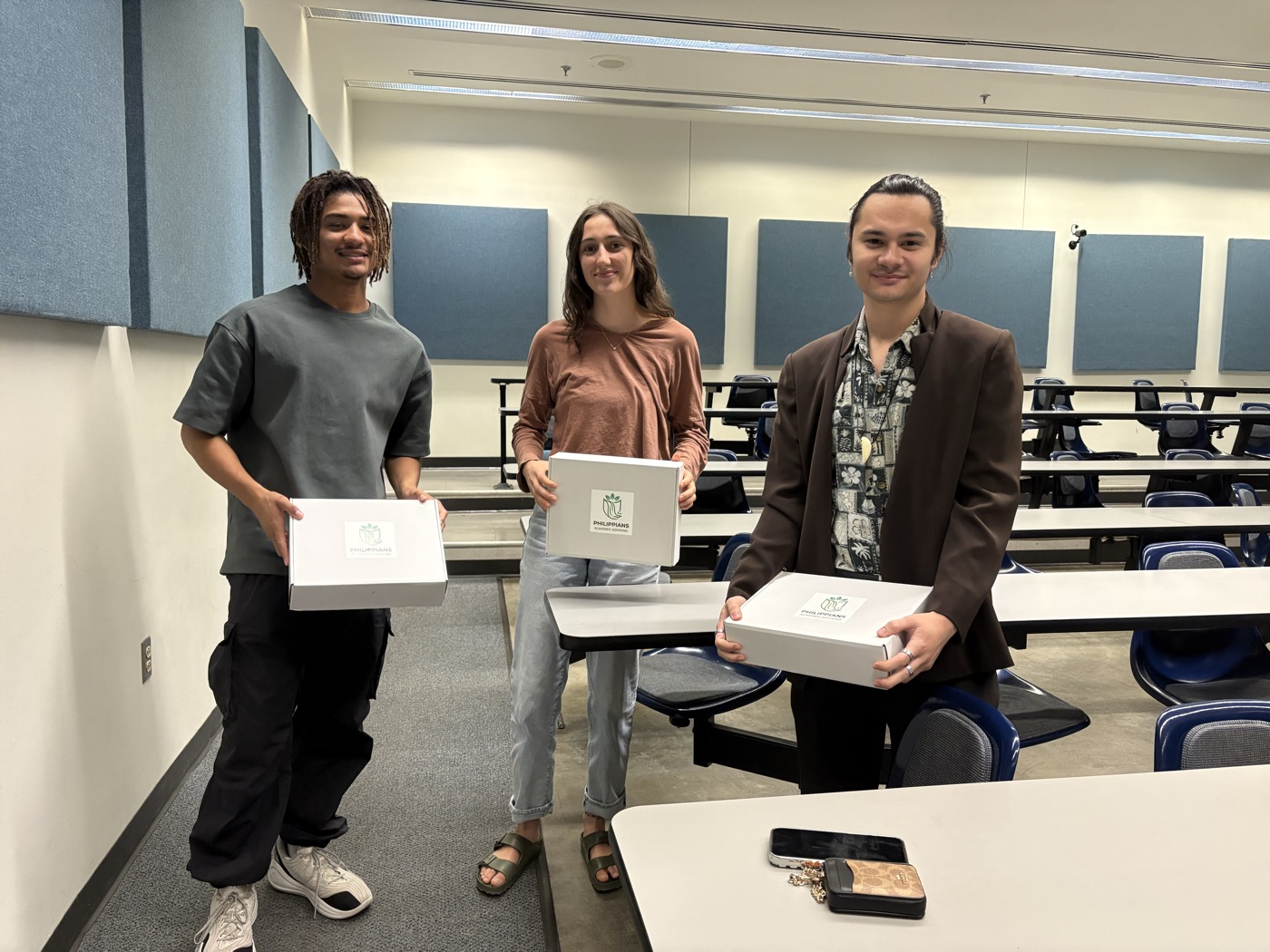 Three pre-med students in a lecture hall, each holding a Philippians giveaway box